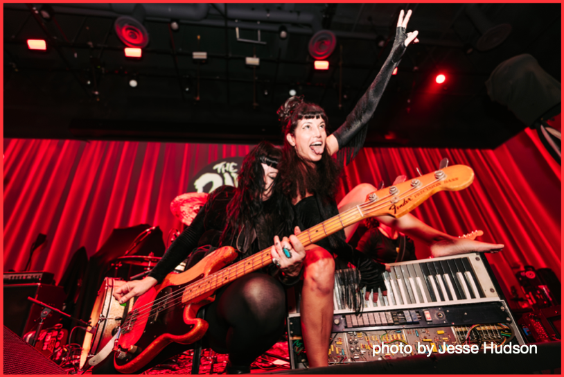 A woman is playing a guitar on a stage in front of a red curtain