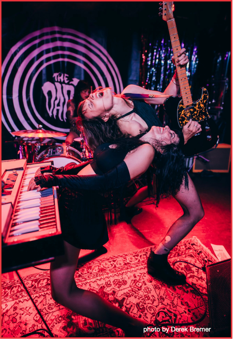 A woman is playing a guitar while another woman is playing a keyboard.