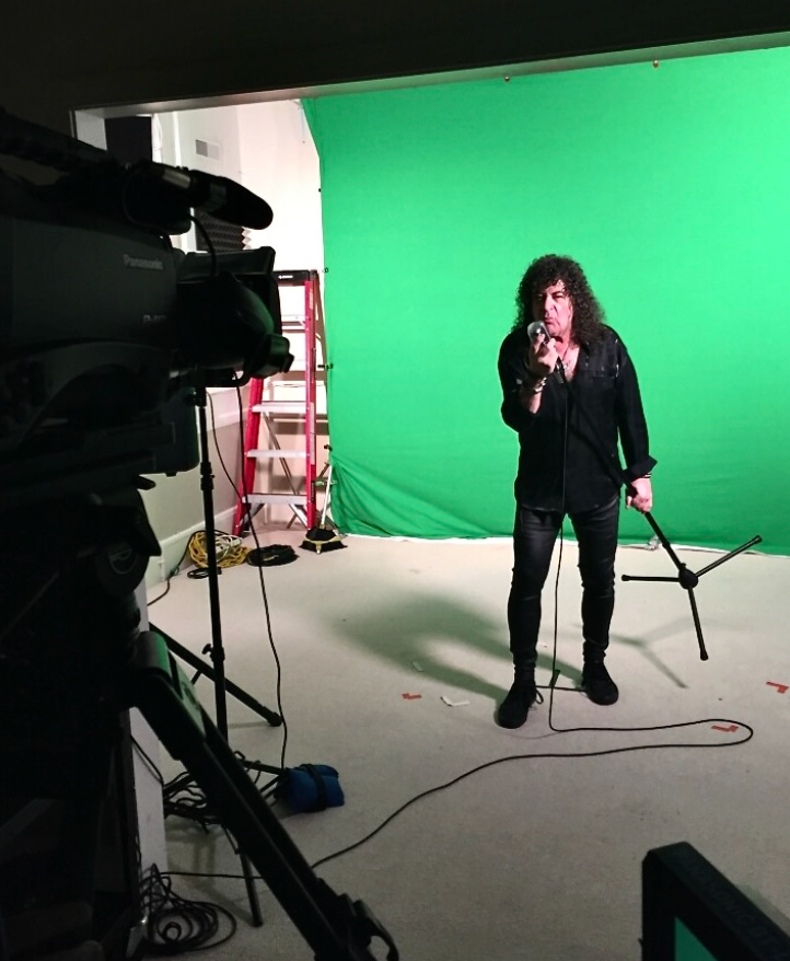 A man singing into a microphone in front of a green screen