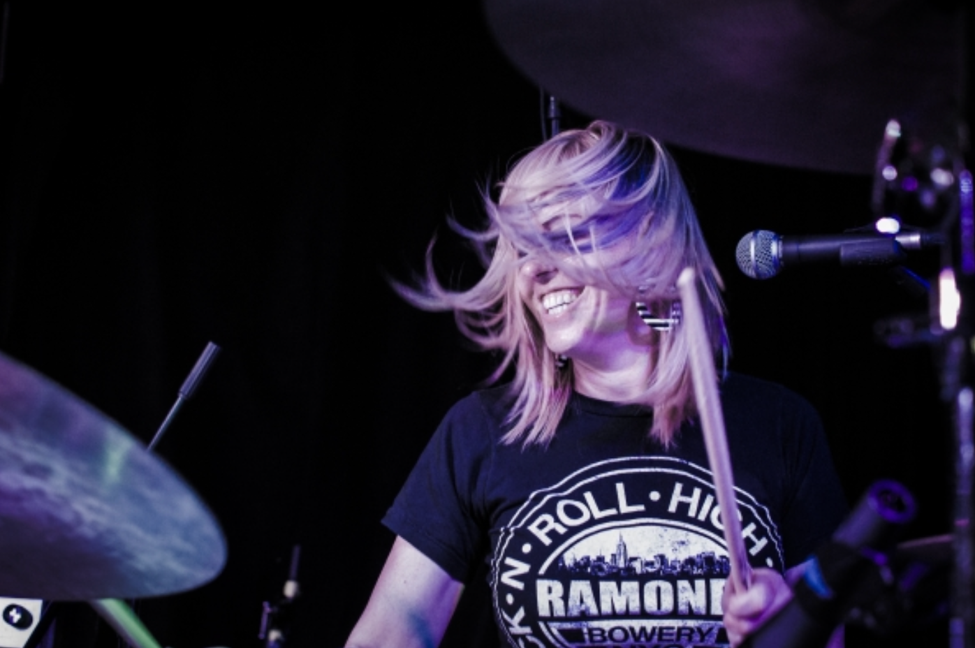 A woman in a ramone shirt is playing drums on a stage.