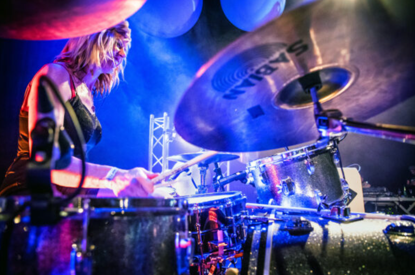 A woman is playing drums on a stage in a dark room.