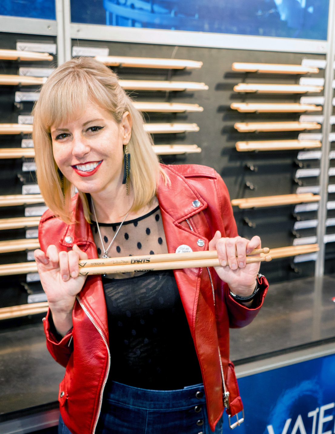 A woman in a red leather jacket is holding a pair of drumsticks.