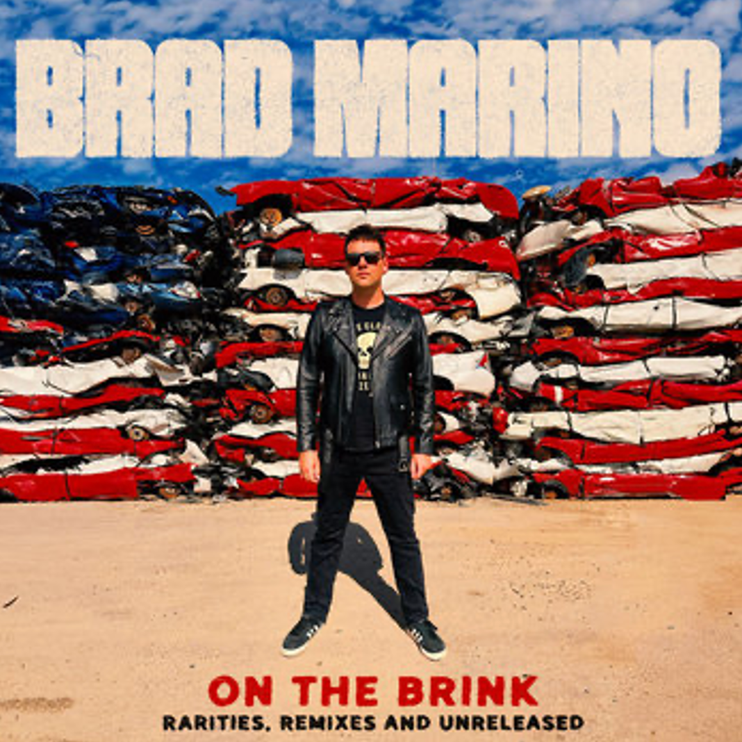 A man in a leather jacket stands in front of an American flag