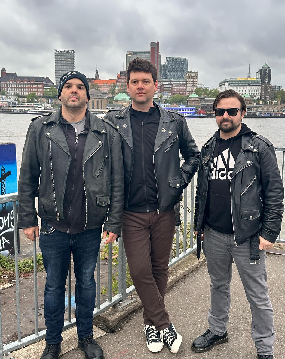 Three men in leather jackets are standing next to each other on a sidewalk.