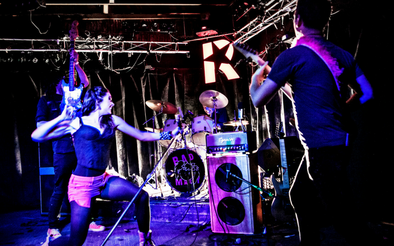 A group of people playing instruments on a stage with the letter k in the background