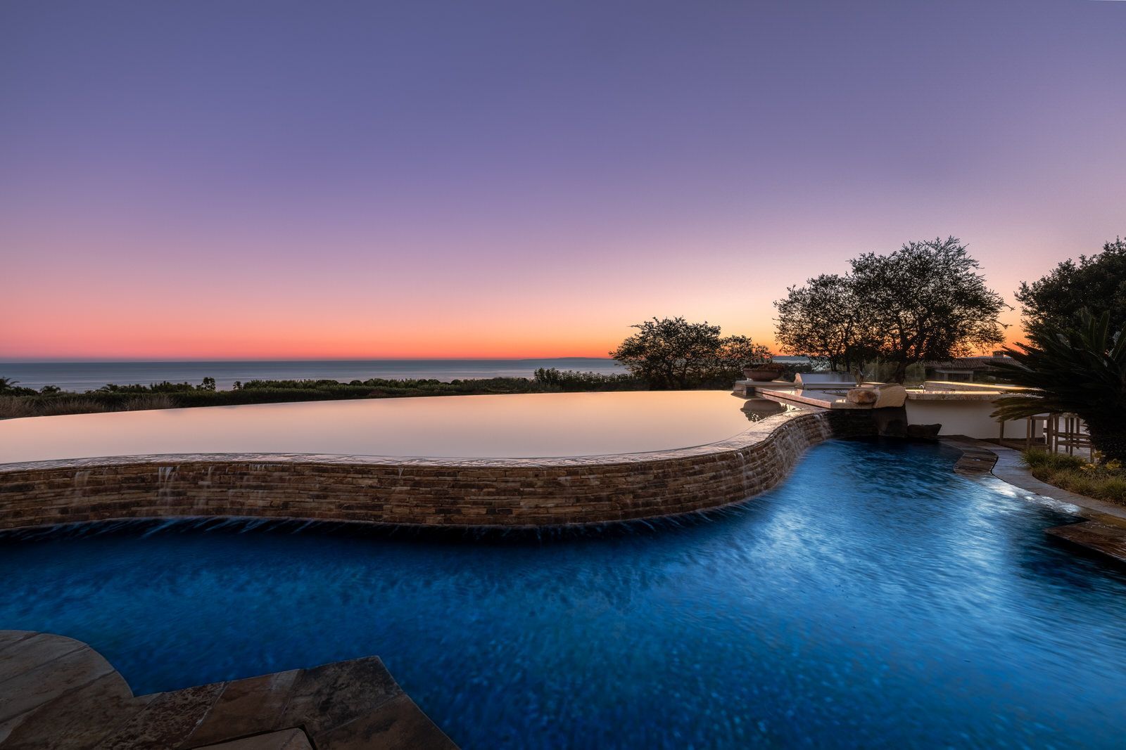 A large swimming pool with a view of the ocean at sunset.