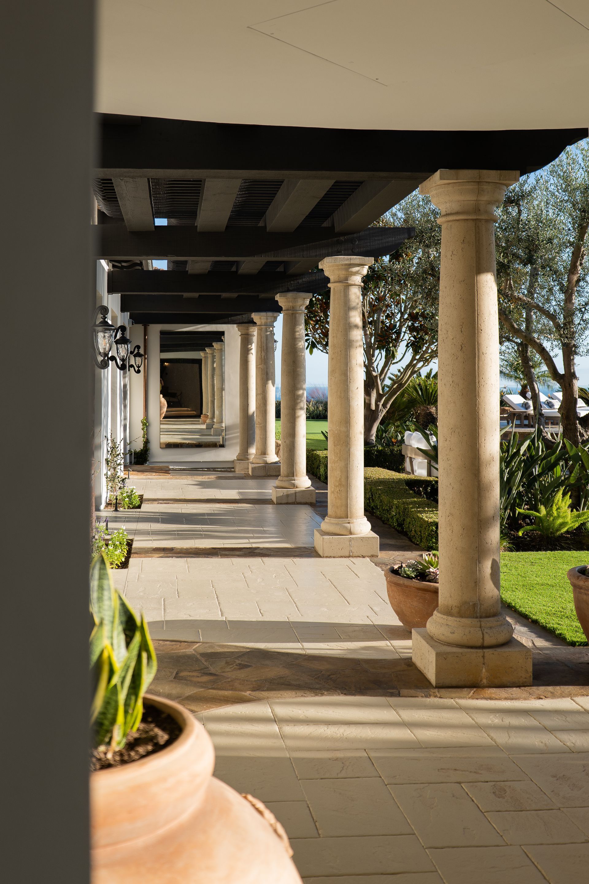 A long walkway with columns and potted plants in front of a building.