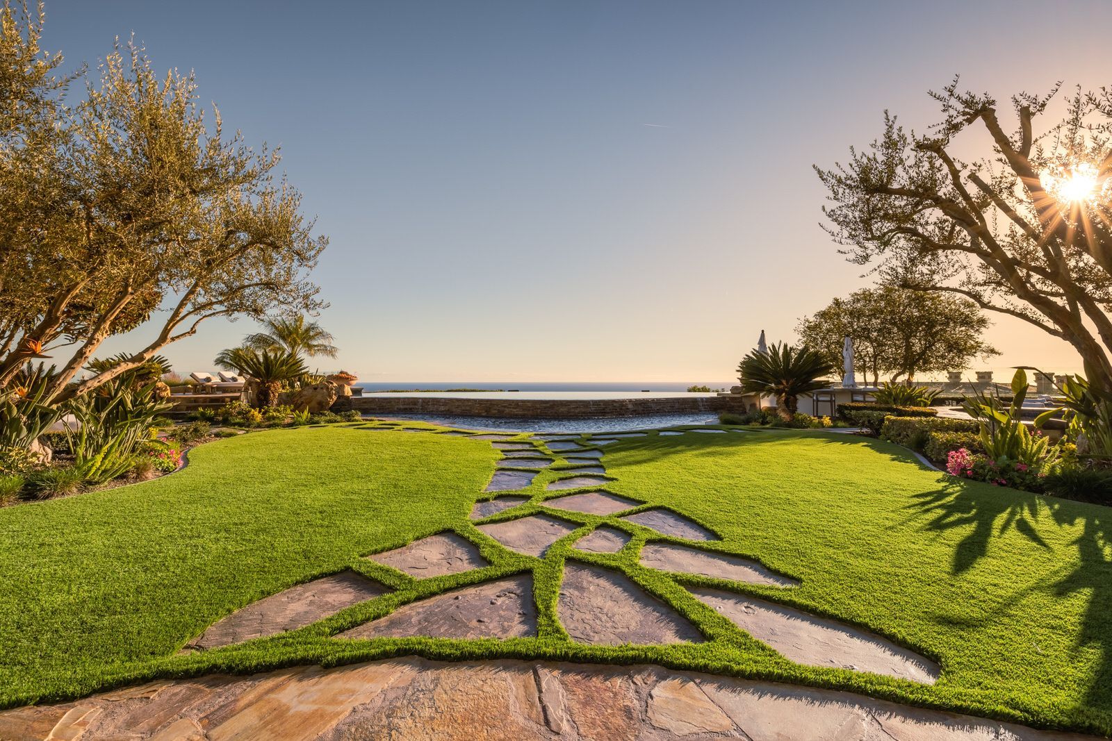 A stone walkway leading to the ocean in a lush green garden.