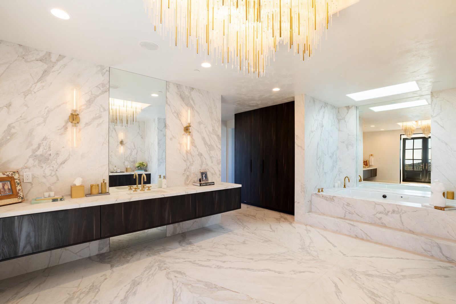 A bathroom with two sinks , a tub , and a chandelier.