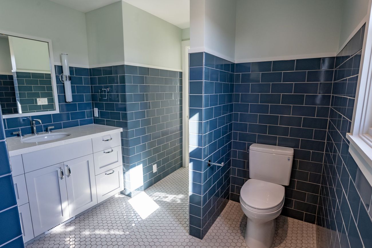 A bathroom with blue tiles , a toilet , a sink and a mirror.