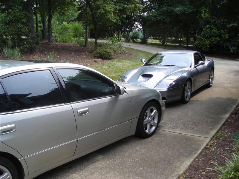 Two silver cars parked on a residential driveway near trees.