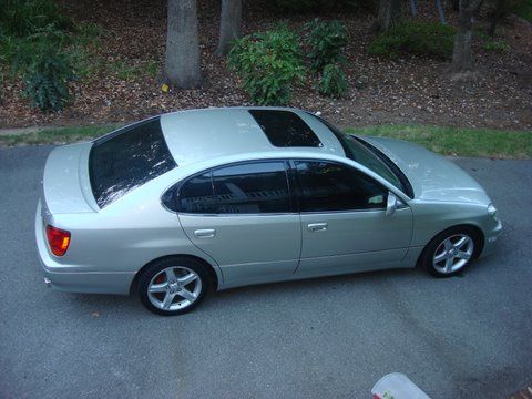 A silver Lexus GS sedan parked on an asphalt driveway next to a grassy area with trees.
