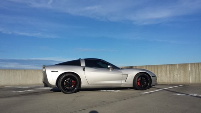 A silver Chevrolet Corvette parked on the top level of a parking garage under a clear blue sky.