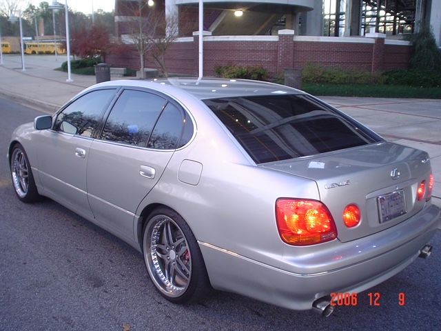 Silver Lexus GS sedan parked on an asphalt street with aftermarket wheels and tinted windows, viewed from the rear.