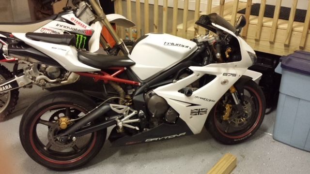 A white Triumph Daytona 675 sportbike parked in a garage next to a dirt bike.