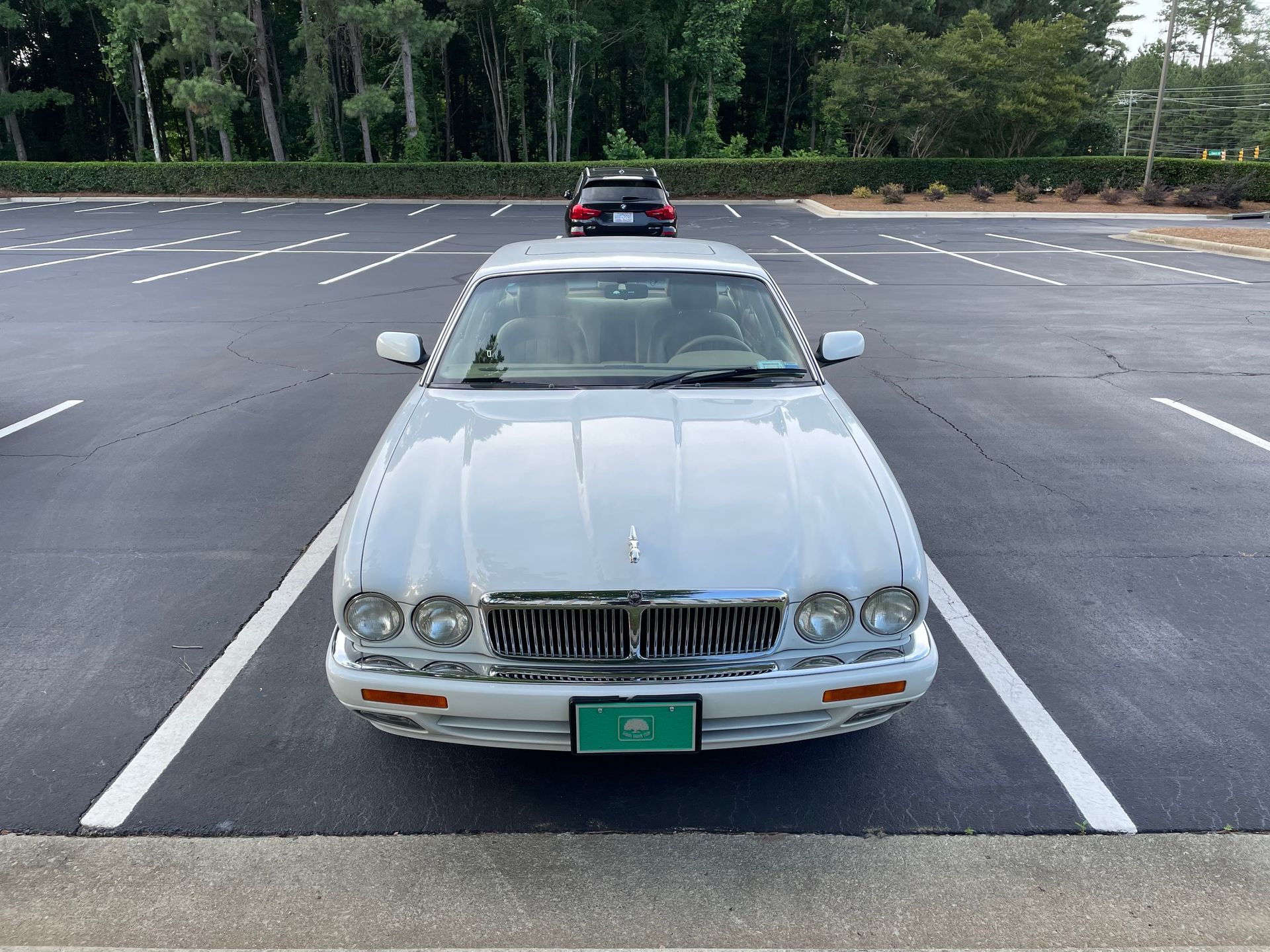 A silver Jaguar sedan parked in an empty outdoor parking lot with a black car visible in the distance.