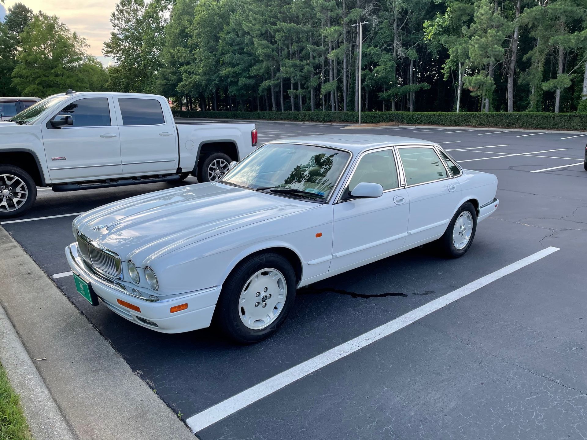 A white Jaguar XJ sedan parked in a parking lot next to a white pickup truck.