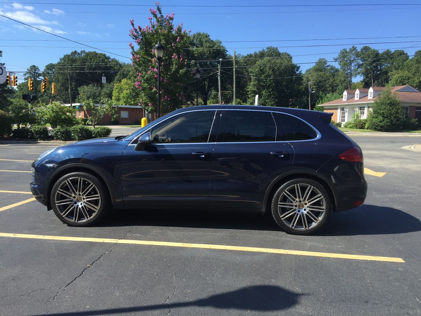 A side view of a dark blue Porsche Cayenne SUV parked in a paved lot on a sunny day.