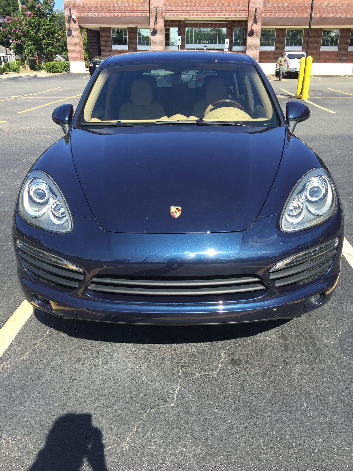 A dark blue Porsche Cayenne SUV parked in an asphalt parking lot in front of a brick building.