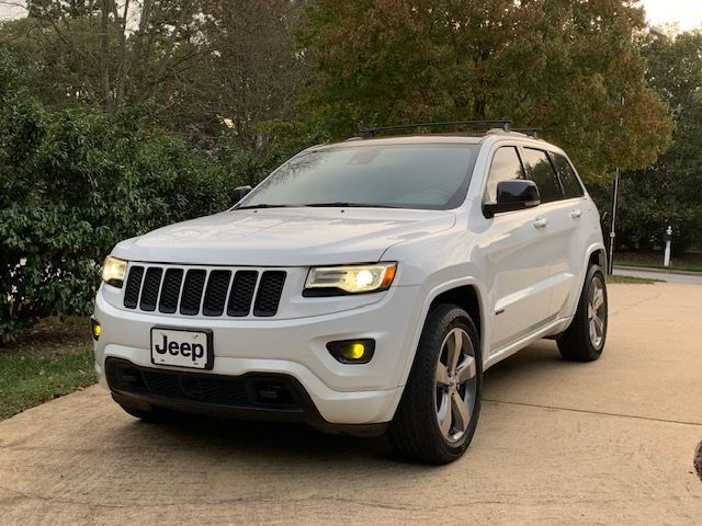 A white Jeep Grand Cherokee parked on a concrete driveway with trees and foliage in the background.