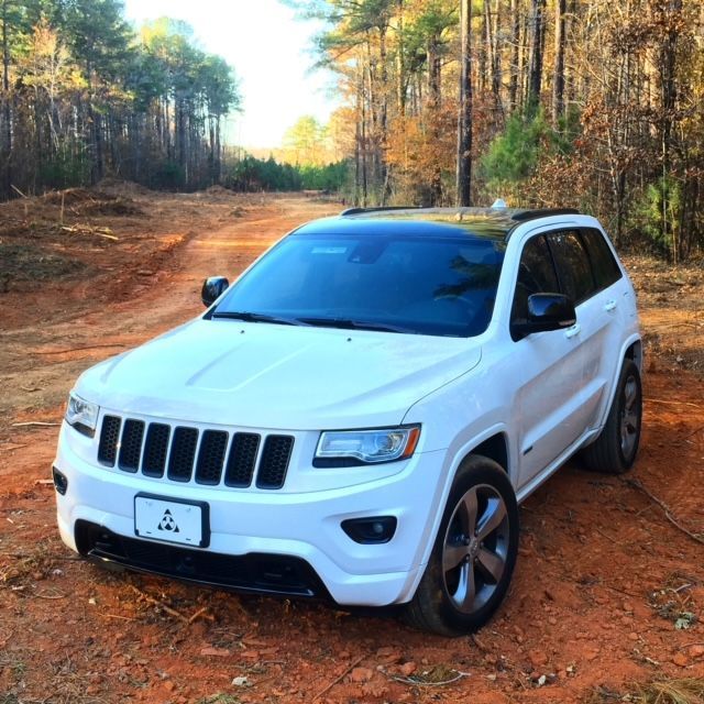 A white Jeep Grand Cherokee parked on a dirt path in a wooded area.
