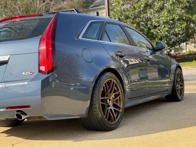 A gray Cadillac CTS-V wagon parked on a paved driveway with custom bronze-colored wheels.
