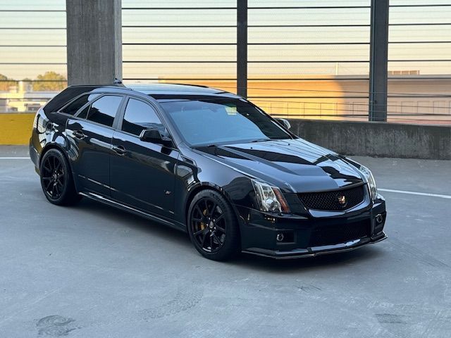 A black Cadillac CTS-V wagon parked on the top level of a multi-story concrete parking garage at sunset.