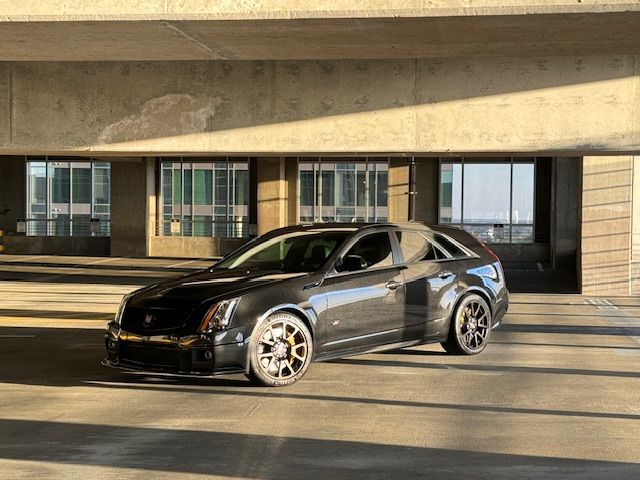 A dark grey Cadillac CTS-V wagon parked inside a concrete parking garage with warm, angled sunlight.