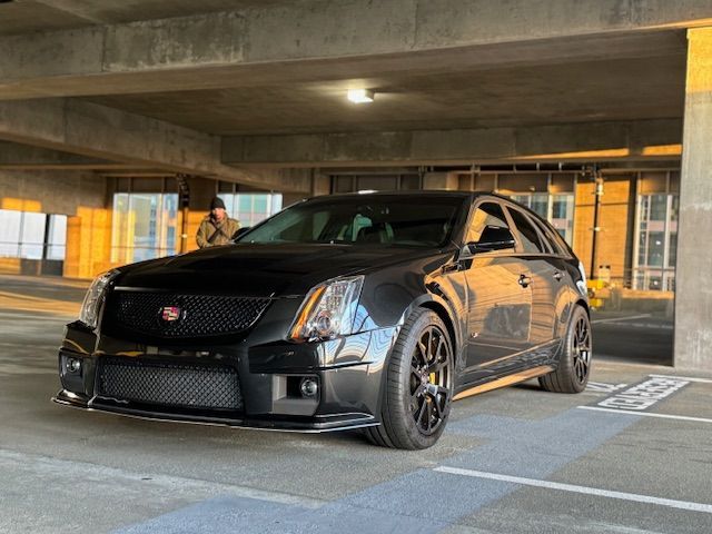 A sleek black Cadillac CTS-V wagon parked inside a concrete parking garage during golden hour.