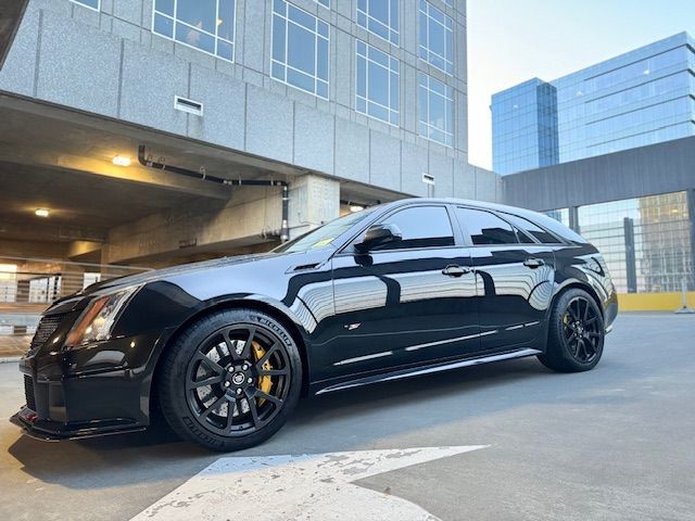A black Cadillac CTS-V wagon parked in an outdoor parking structure during the day.