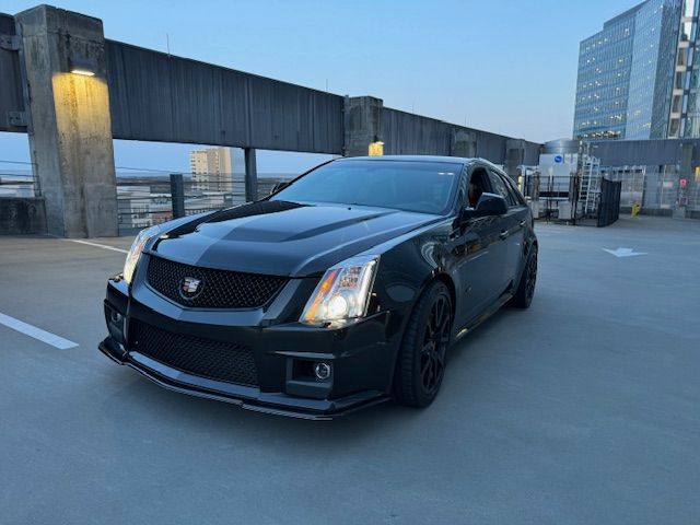 A black Cadillac CTS-V parked on the top level of a concrete parking garage at dusk.