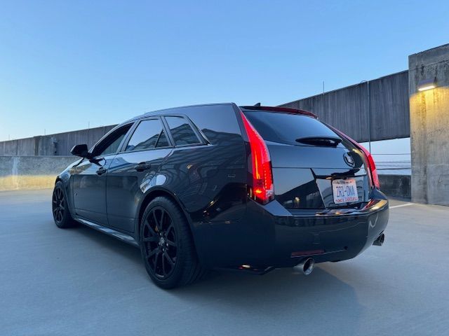 A black Cadillac CTS station wagon parked on the top level of a concrete parking garage under a clear blue sky.
