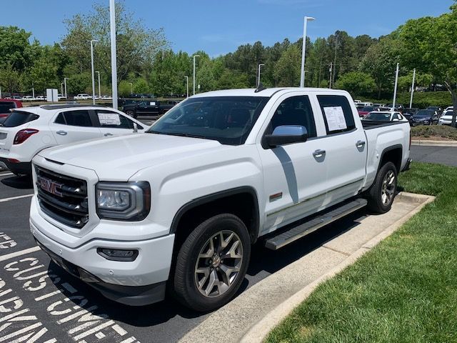 A white GMC crew cab pickup truck parked in a sunny dealership lot with other vehicles visible in the background.