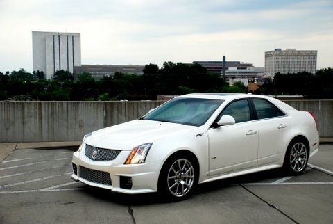 A white Cadillac CTS-V sedan parked on a rooftop lot with large buildings in the background.
