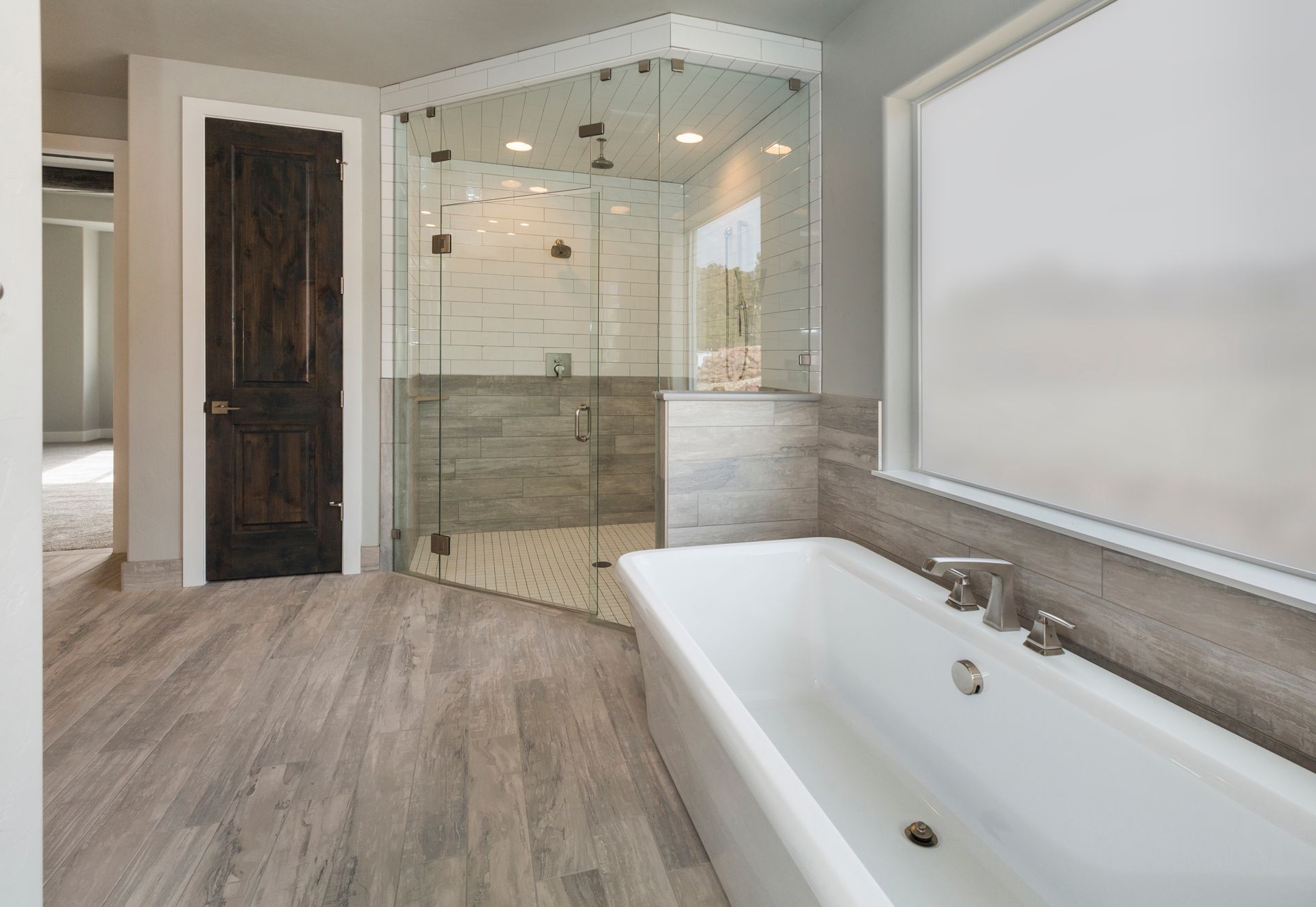 Modern bathroom with gray wood-look floors, a white freestanding tub, and a glass-enclosed walk-in tile shower.