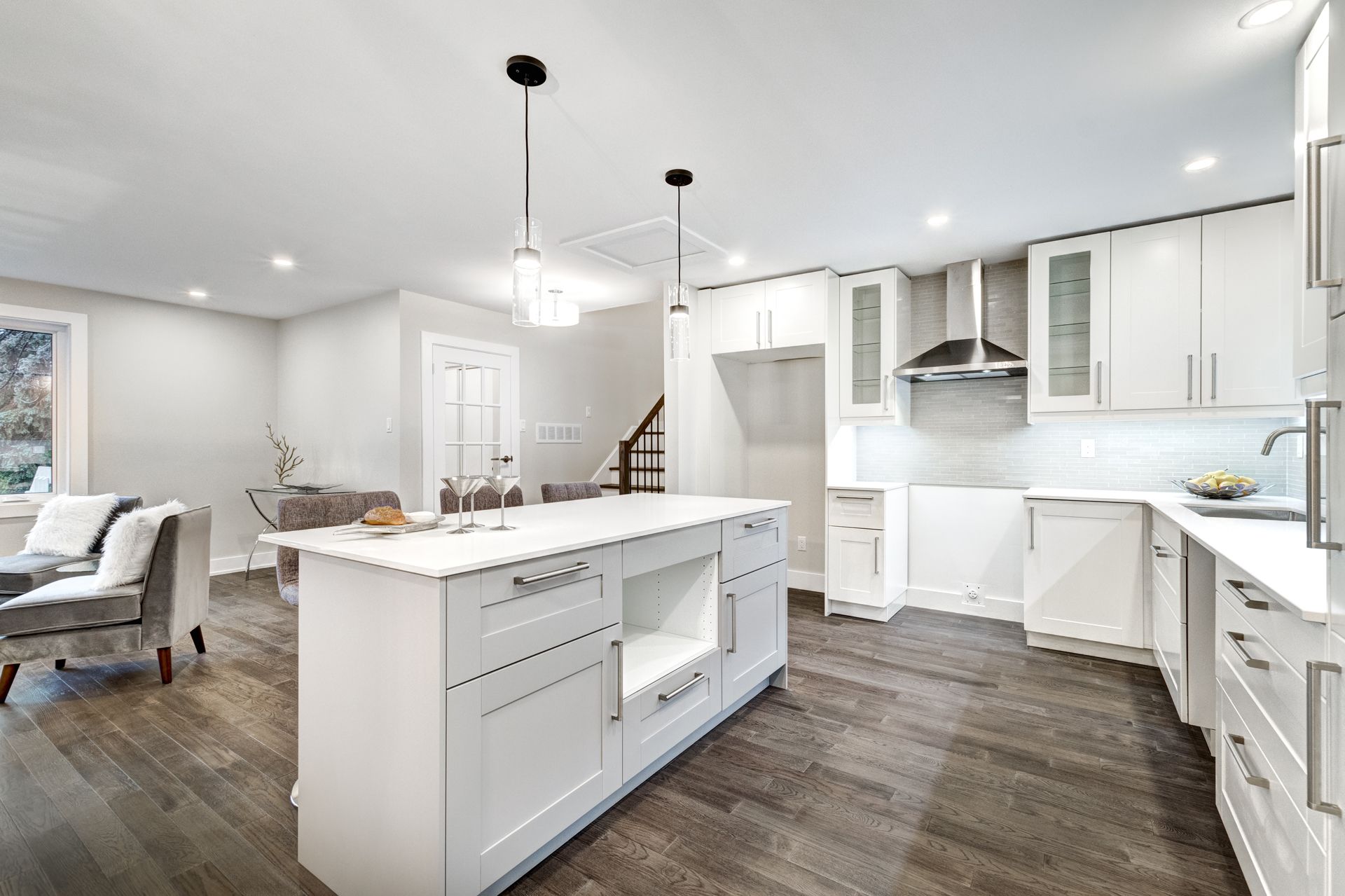 A modern, open-concept kitchen with white cabinets, a central island, and wood-style flooring, adjoining a living area.