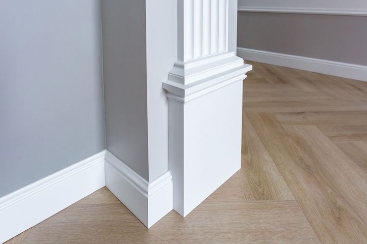 White architectural molding and baseboards transition from a gray wall to a corner, set against light wood flooring.