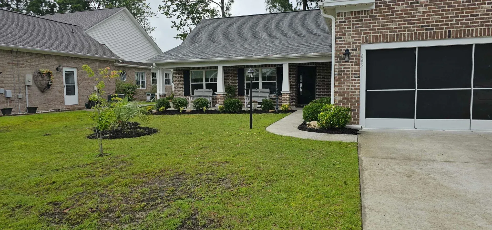 A residential house with a green lawn, brick facade, and black garage screen.