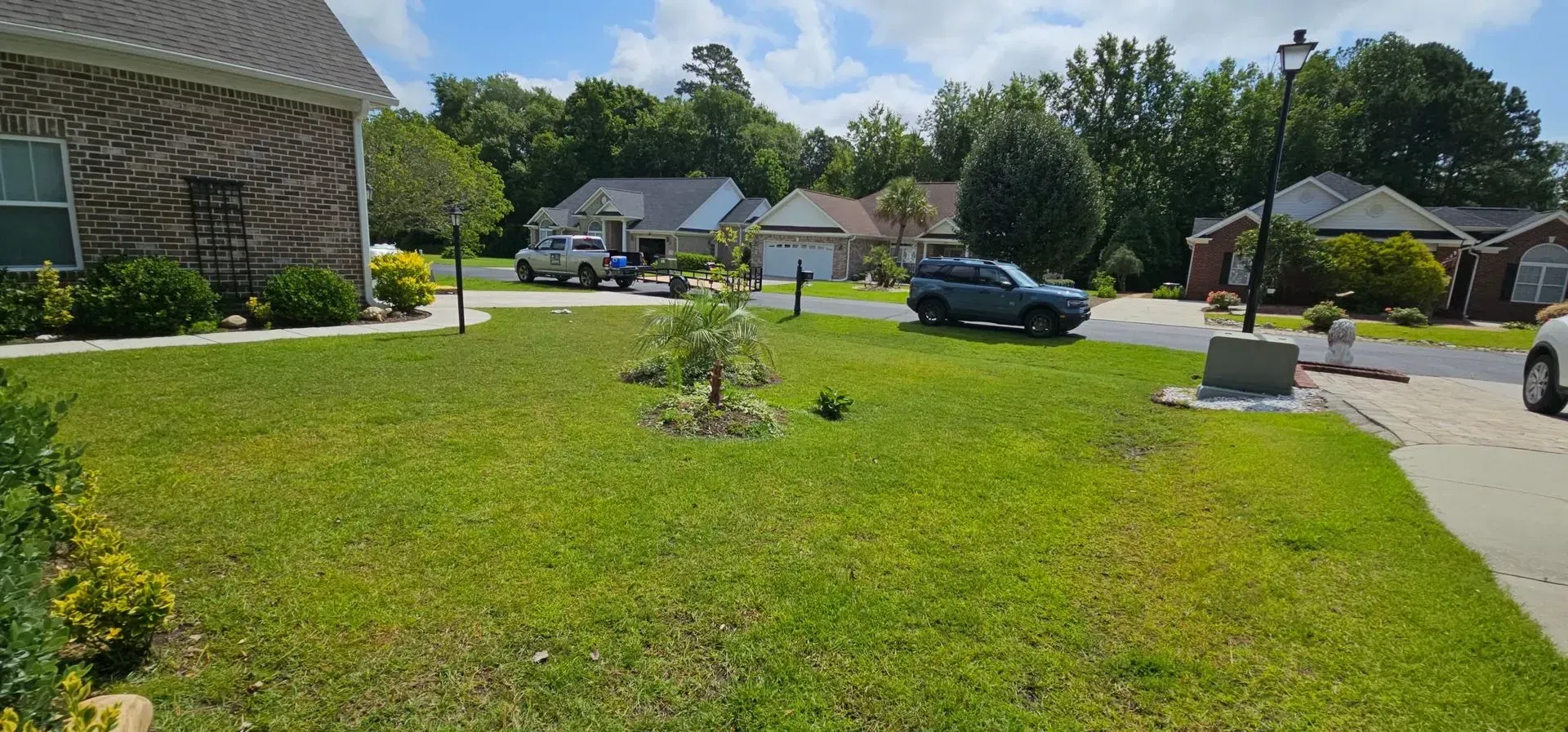 Suburban houses with green lawns and trees on a sunny day. A car is parked in the driveway.