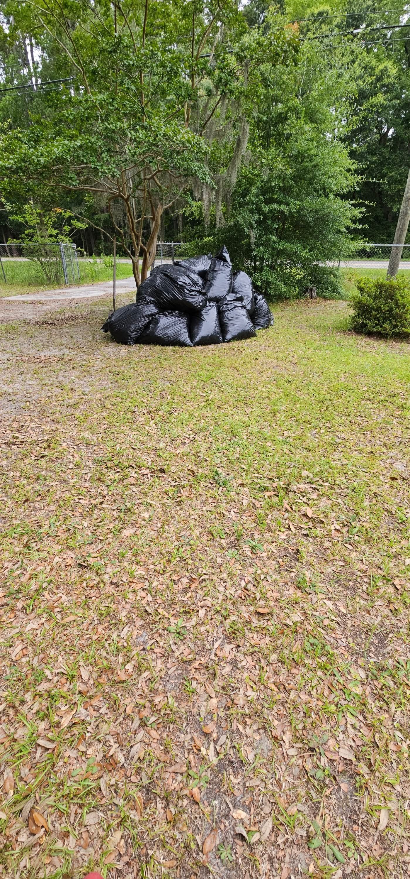 Pile of black trash bags on a grassy lawn with trees in the background.