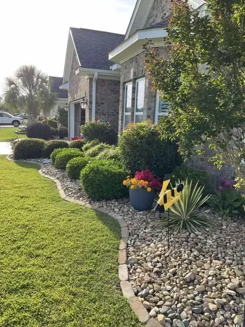 Well-manicured front yard with green grass, a curved flowerbed, and a brick house.