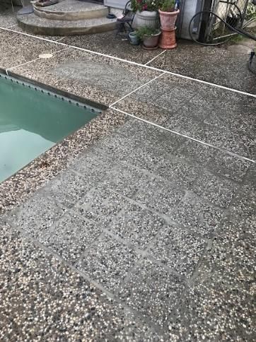 A concrete patio next to a swimming pool with potted plants.