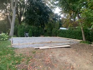 Une allée en béton est en cours de construction dans une cour arrière entourée d'arbres.