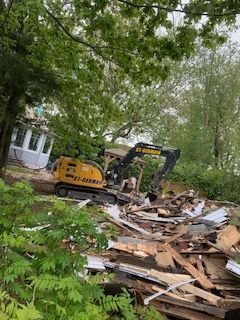 Une excavatrice jaune démolit une maison dans les bois.