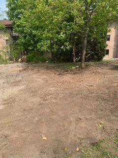 Un champ de terre avec des arbres en arrière-plan et un bâtiment en arrière-plan.