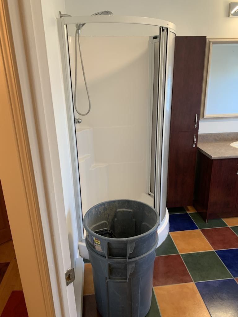 Une poubelle grise se trouve à côté d'une cabine de douche dans une salle de bain.