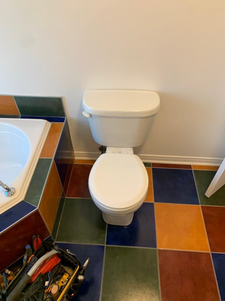 Une toilette est posée sur un sol carrelé dans une salle de bain à côté d'une baignoire.