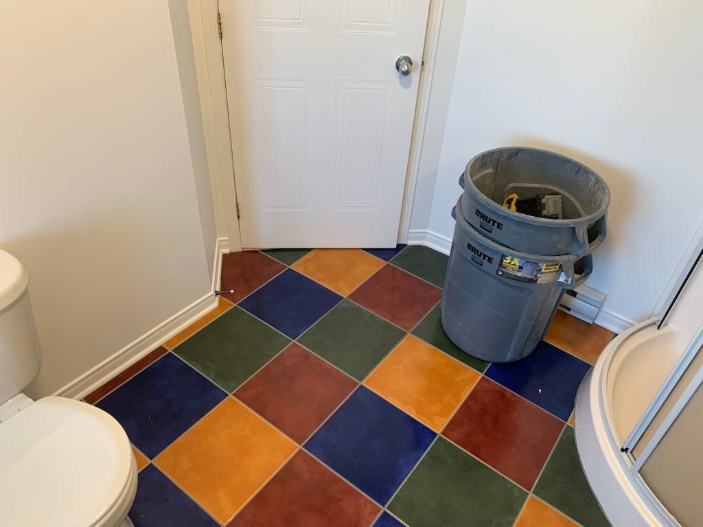 Une salle de bain avec un sol carrelé coloré, des toilettes et une poubelle.