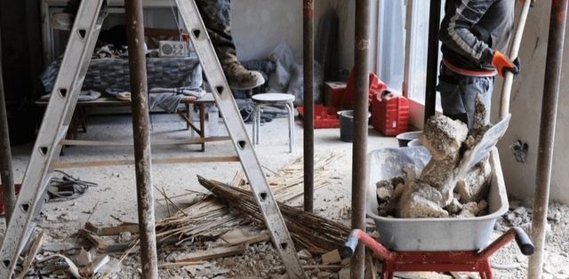 Un homme se tient debout sur une échelle à côté d'une brouette remplie de pierres.
