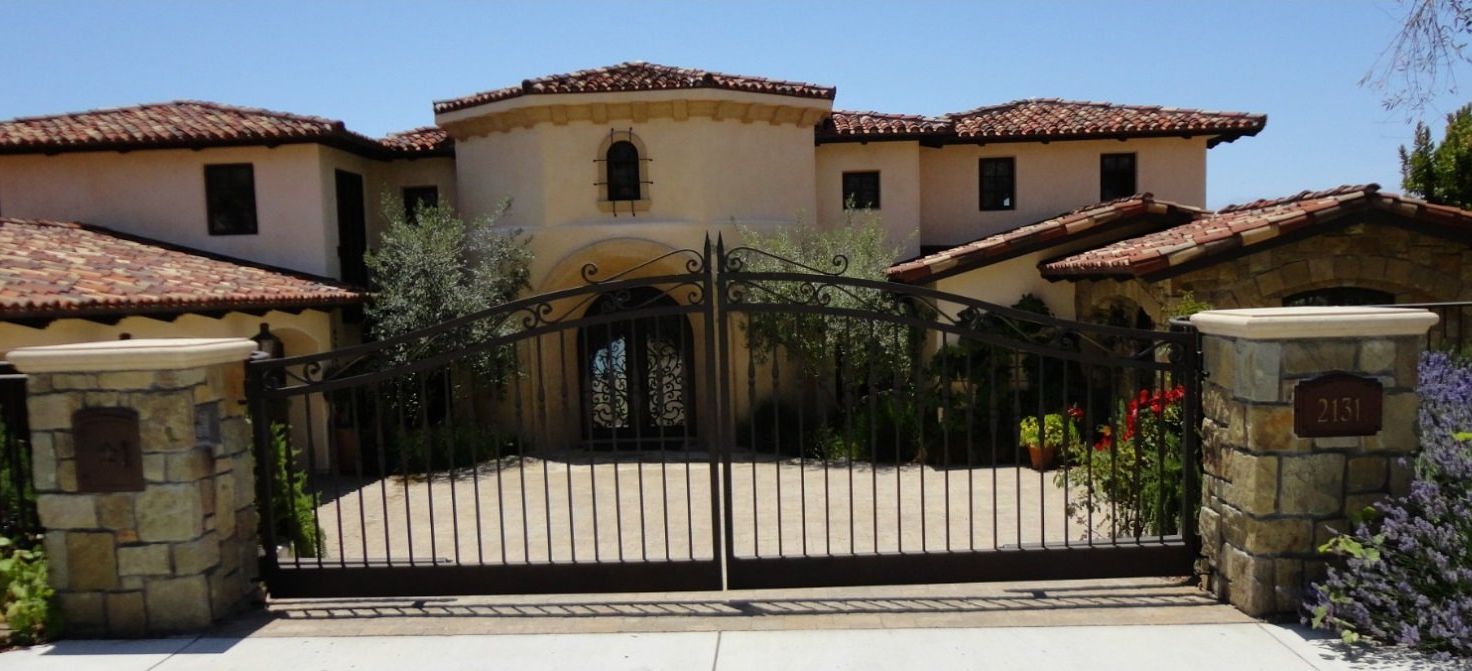 Luxurious house with brown tile roof, stone gate posts, and a wrought iron gate.